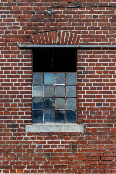 Broken damaged industrial window with a rusted metal frame, some parts are white painted, on a red brick wall, use as game texture asset