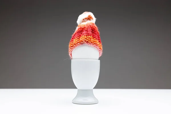 yumurta ve kırmızı turuncu ev yapımı yün şapka beyaz bir masada koyu gri arka plan, fotokopi metni için yer veya Paskalya veya Noel için tebrik kartları