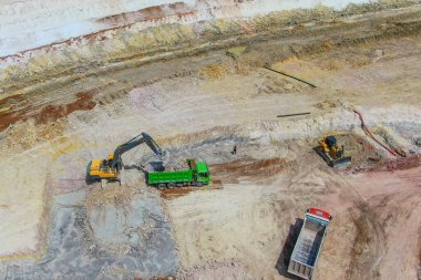 Taş ocağında mavi kil çıkarma işlemi. Kil özütü. Bir kazıcı mavi kil çıkarıp yeşil bir kamyona yüklüyor. İHA fotoğrafı. Kuş gözü.