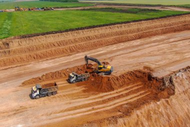 Kil çıkarma için taş ocağı inşaatı. Aşırı yük işe yarıyor. Kazıcı toprağı kil çıkarmak için kırıyor ve iki gri kamyona yüklüyor. İHA fotoğrafı. hava görünümü