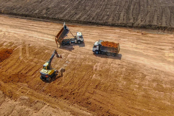 overburden works. quarry development for clay extraction.   excavator breaks up the topsoil to extract clay and loads into grey truck. drone photo.