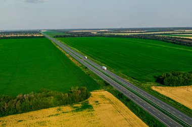 kargo teslimatı İki beyaz kamyon ve kargo yeşil tarlalar boyunca asfalt yolda ilerliyor. Havadan görüldü. Havadan arka plan manzarası. Drone fotoğrafçılığı. 