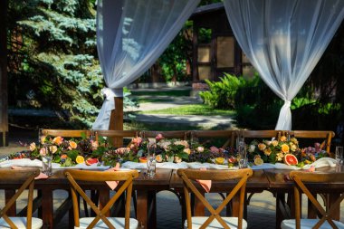 Açık hava restoranında düğün kutlaması için güzel bir masa. Taze çiçekler ve meyvelerle süslenmiş..