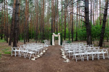 Çam ormanında düğün töreni. Açık havada yapılacak bir düğün için şık bir dekorasyon. Güzel beyaz mobilyaları olan açık hava düğün töreni. Tahta misafir sandalyeleri..