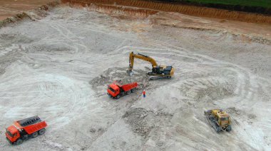 Mavi killi panorama ocağı. Sarı kazıcı kil çıkarır ve kırmızı kamyonlara yükler. Drone görünümü