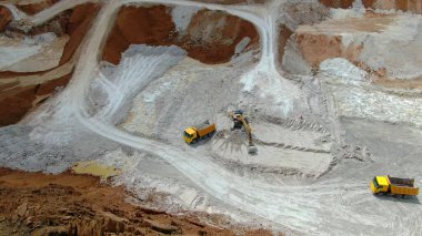 Mavi killi panorama ocağı. Sarı kazıcı, sarı kamyonetteki kil yığınlarını çıkarıyor. Drone görünümü
