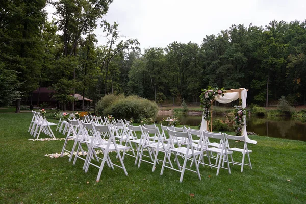 Wedding ceremony in the forest. Elegant decoration of a wedding ceremony outdoors. Outdoor wedding ceremony with beautiful white furniture. Wooden guest chairs.