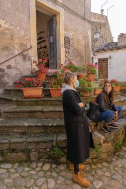 Calcata Vecchia, İtalya - 20 Ekim 2020, Maskeli insanlar bir sürü Calcata Vecchia çiçeğiyle taş basamaklarda. Koronavirüsün ikinci dalgası (covid19), sosyal mesafeyi koruyor
