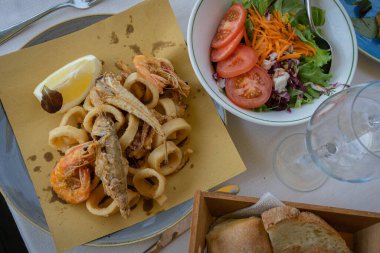 Çeşitli kızarmış balık, kalamar, karides, karışık salata ve ekmek görüntüsü