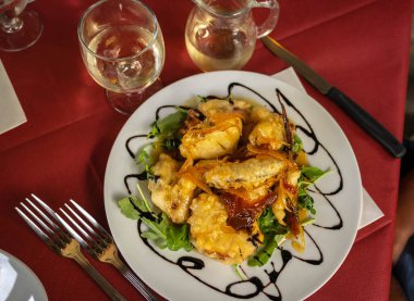 Mangır içinde ahtapot resmi ve İtalya 'da kırmızı bir masa örtüsünde beyaz bir tabakta kurutulmuş portakal sosu.