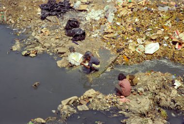 Kathmandu, Nepal - Apr 18, 1997: Two Nepalese are looking for something to sell in a trashy river. Nepal was one of the poorest countries in the world. clipart