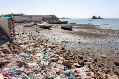 Plajda plastik torbalar ve PET şişeleri etrafa saçılmış.