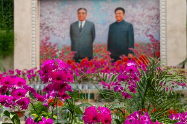 Pyongyang, Kuzey Kore - 16 Nisan 2010: Begonya çiçekleriyle çevrili Kim Il Sung ve Kim Jong Il 'in portresi