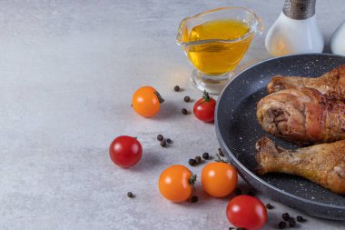 Gri mutfak masasında çiğ tavuk, baharat ve olgun domates.