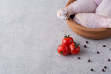 Gri mutfak masasında çiğ tavuk, baharat ve olgun domates.