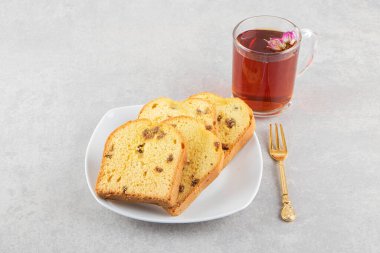 Bir fincan çay ve gri arka planda kuru üzümlü dilimlenmiş ekmek.