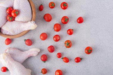 Gri mutfak masasında çiğ tavuk, baharat ve olgun domates.