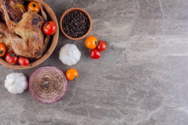 Gri mutfak masasında çiğ tavuk, baharat ve olgun domates.