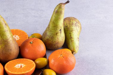 Taze armutlar, kumkatlar ve gri arka planda mandalinalar. 