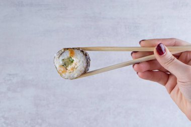 Kadın elinde yemek çubuklarıyla suşi rulosu tutuyor.