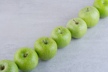 Gri bir masada yeşil elma sırası