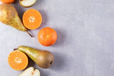 Gri bir zemin üzerinde taze armutlar ve mandalinalar. 