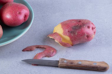 Gri arka planda olgun kırmızı patatesler ve bıçak.