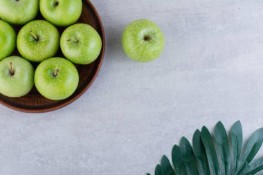 Gri bir masada, kil tabakta yeşil elmalar