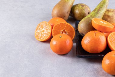 Gri bir zemin üzerinde taze armutlar ve mandalinalar. 