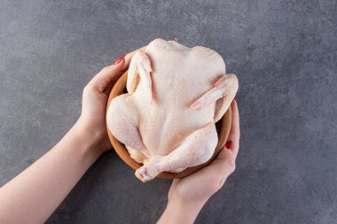 Kadın elleri, gri arka planda bir kasede çiğ tavuk tutuyor.
