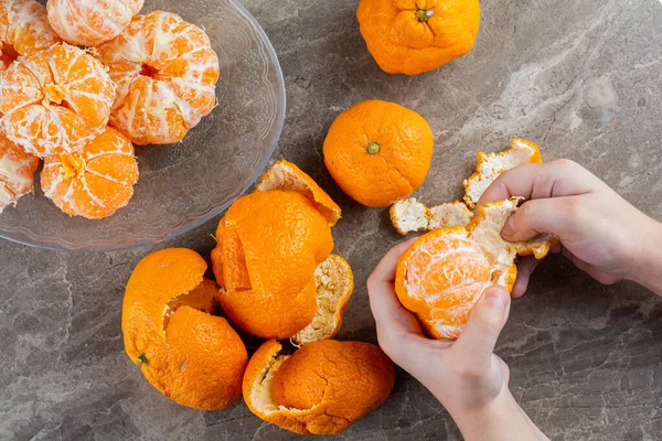 hands peeling  tangerine on a gray background.