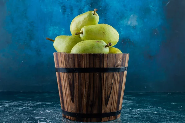 ripe green pears in a wooden bucket on a dark background.