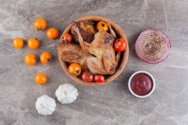 Gri mutfak masasında çiğ tavuk, baharat ve olgun domates.