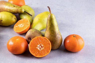 Gri bir zemin üzerinde taze armutlar ve mandalinalar. 