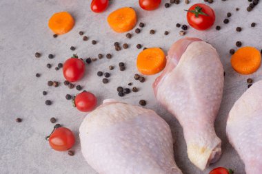 Gri mutfak masasında çiğ tavuk, baharat ve olgun domates.