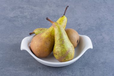 Olgun yeşil armutlar gri bir zemin üzerinde kil plaka. 