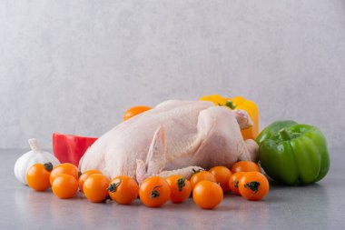 Gri mutfak masasında çiğ tavuk, baharat ve olgun domates.