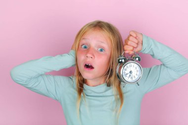Liseli kız sabah erken kalkmaktan nefret eder. Alarm saati tutan sarışın kız pembe arka planda kulağını kapatıyor.