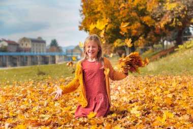 Sonbahar parkında düşen sarı yapraklarla oynayan mutlu küçük kız. Kızlar açık havayı sever. Sonbahar sonbahar havası.