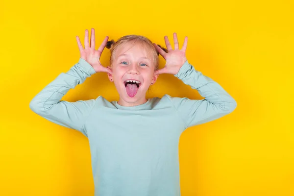 Érzelmes lány. Vicces kislány mutatja nyelv sárga háttér. Érzelmek a gyerek arcán. Boldog gyermekkori koncepció — Stock Fotó