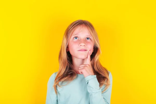 Fiatal lány sárga háttér gondolkodás egy ötlet. kéz az állon gondolkodva a kérdésen. Kétség, ötlet koncepció. — Stock Fotó