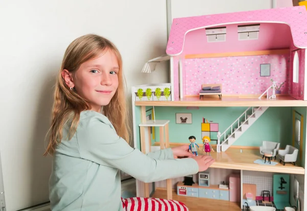 Szczęśliwa dziewczyna bawi się domkiem dla lalek i lalkami. Szczęśliwe dziecko. — Zdjęcie stockowe