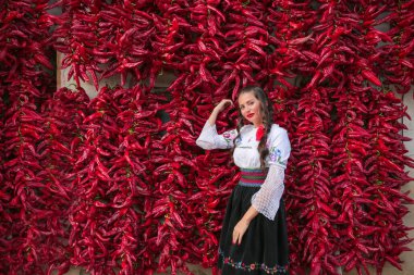 Geleneksel Sırp kıyafetleri, ulusal halk kostümleri giymiş genç bir kadın. Kırmızı biber arsasının yakınında poz veriyor.