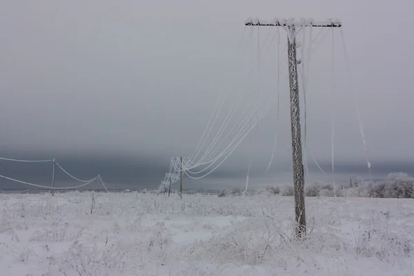 Líneas eléctricas de fase rota con escarcha en los postes eléctricos de madera en el campo en el invierno después de la tormenta — Foto de Stock