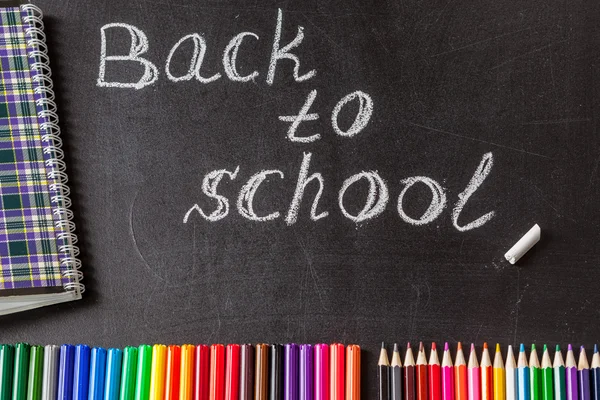 Retour à l'école avec des stylos feutres colorés, crayons, carnet et le titre "Retour à l'école" écrit à la craie blanche sur le tableau — Photo