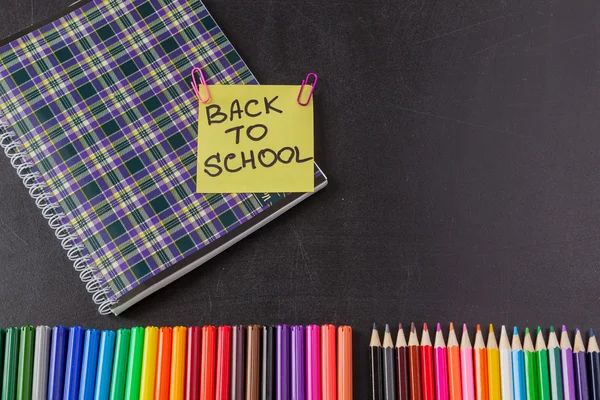 Повернутися до шкільного фону з барвистими ручками для кінчиків, олівцями, блокнотом та заголовком "Назад до школи", написаними на жовтому аркуші паперу на крейдовій дошці — стокове фото