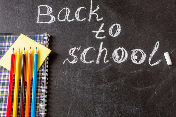 Back to school background with title "Back to school" written by white chalk and the notebook with colorful pencils on the chalkboard — стоковое фото