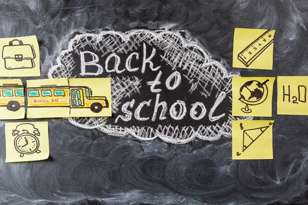 Retour à l'école avec le titre "Retour à l'école" écrit à la craie blanche sur le tableau et le bus scolaire dessiné sur des morceaux de papier jaunes — Photo