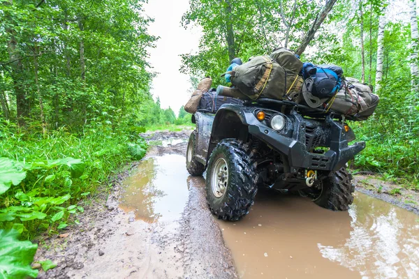 El sucio ATV está con bolsas y cosas en el charco fangoso profundo en el camino del bosque —  Fotos de Stock