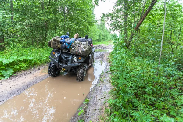 El sucio ATV está con bolsas y cosas en el charco fangoso profundo en el camino del bosque — Foto de Stock